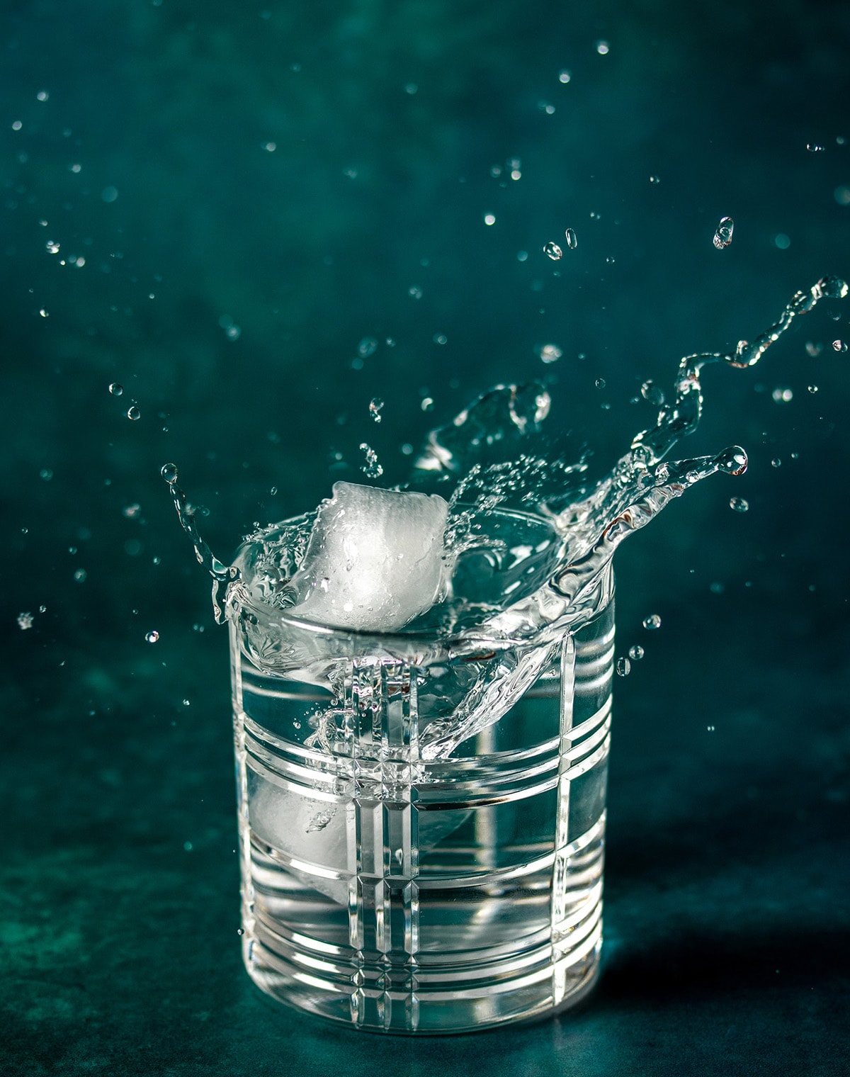 A piece of ice splashing into a glass of water with a green background.