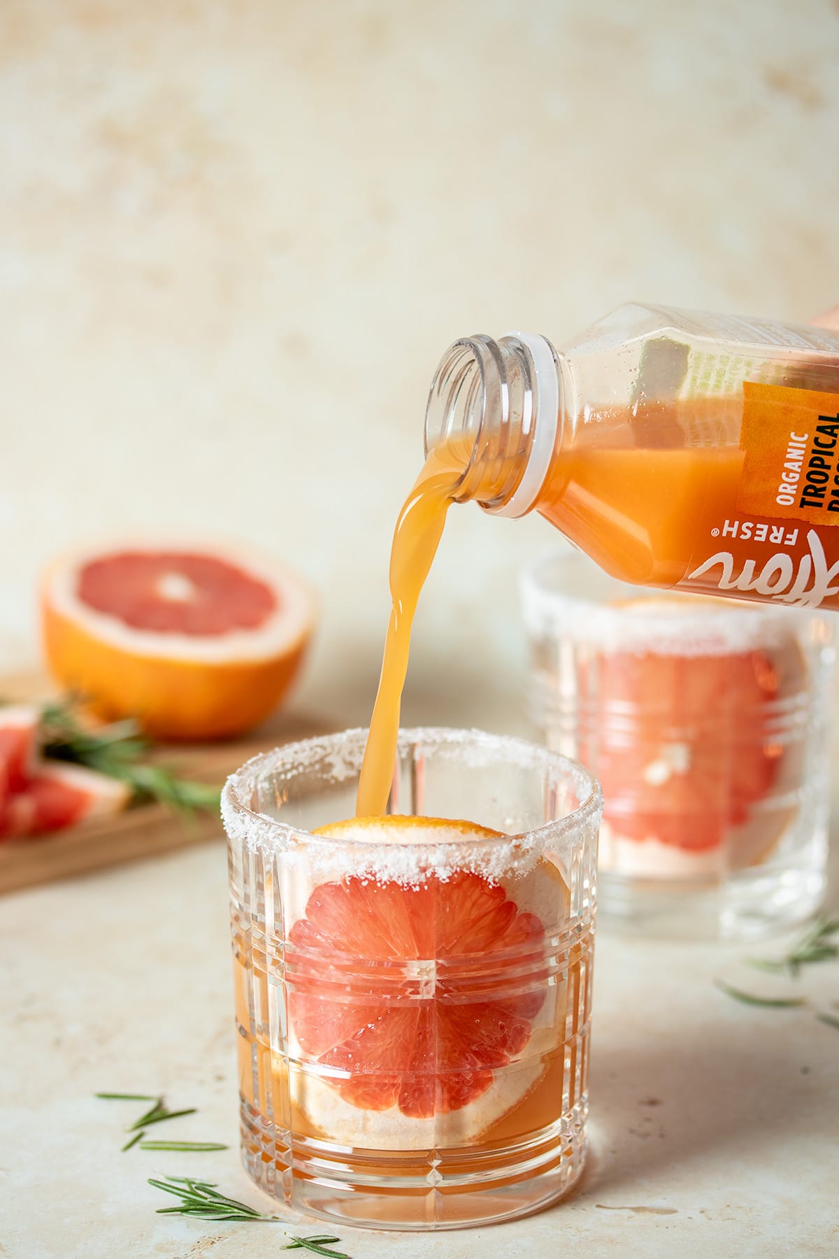 Clear bottle of juice pouring into a glass with a round grapefruit slice stuck to the front of it.